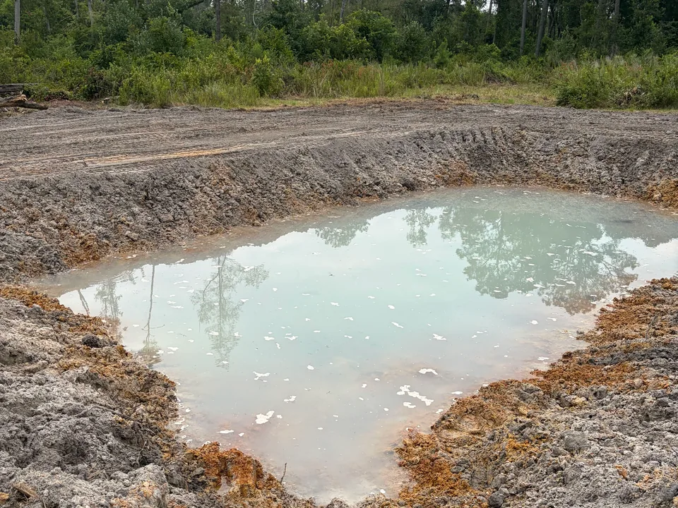 Close view of a freshly dug pit with standing water and clay sides, excavation