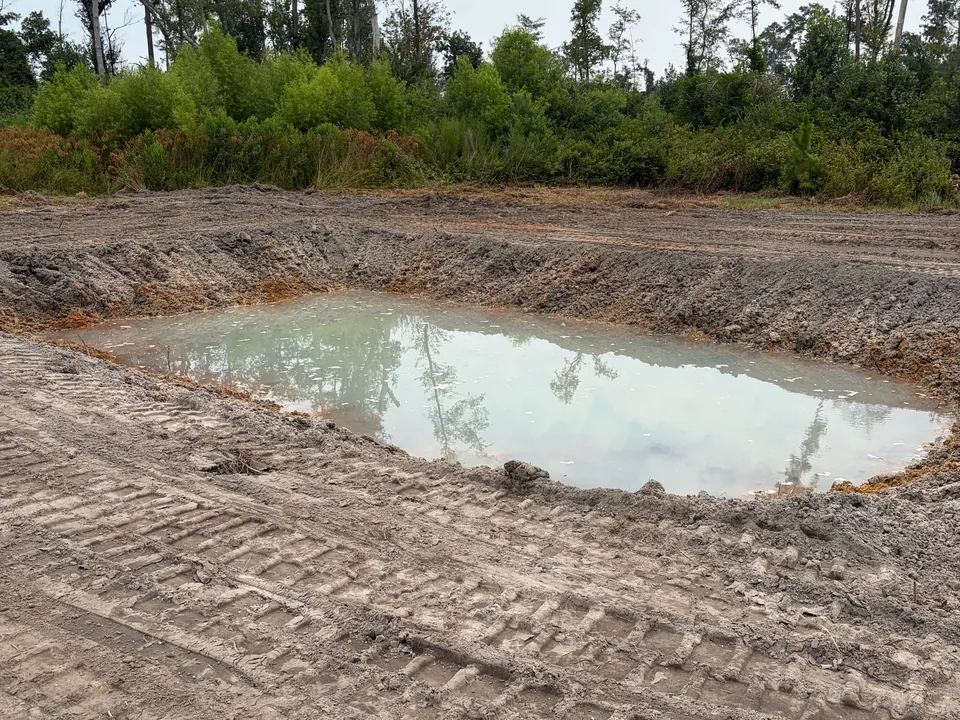 Freshly dug pit holding water with track marks in the dirt, excavation