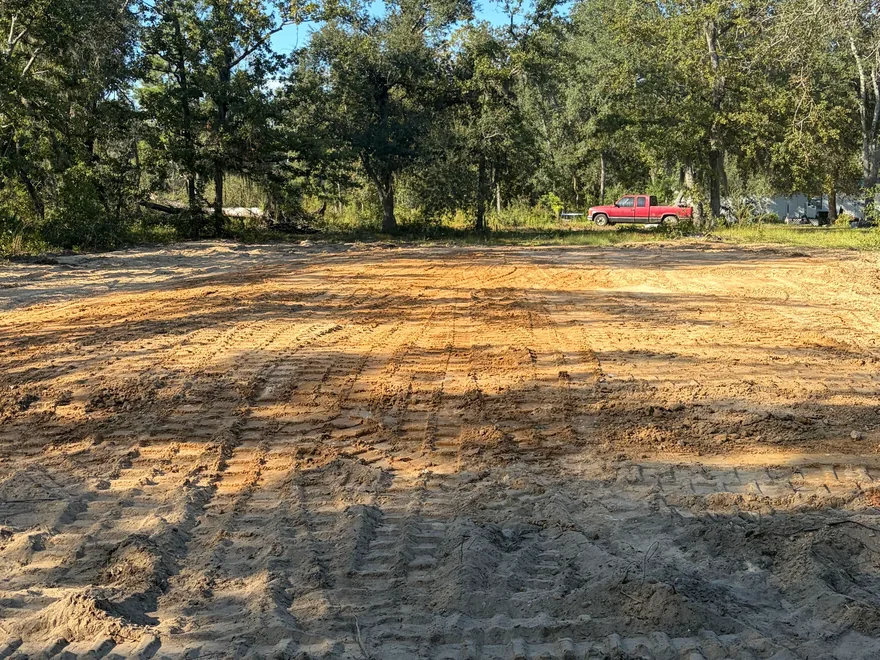 Graded sand pad with fresh track marks in a cleared lot, mobile home pad